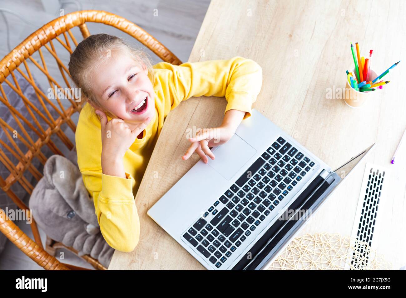 Caucasienne heureuse fille de 10-11 ans est assise dans un fauteuil en osier à un bureau, à côté d'un ordinateur portable, montre un geste - appelez-moi, vue de dessus. Aide à la fatigue oculaire Banque D'Images