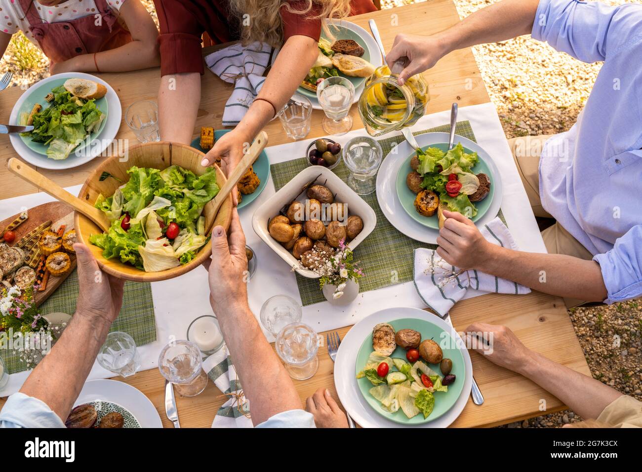Les mains des personnes qui mangent des pommes de terre cuites au four, de la salade de légumes et des légumes grillés au dîner en famille Banque D'Images