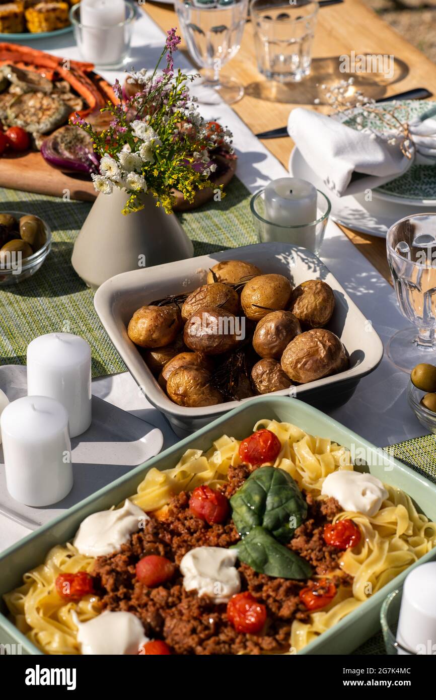 Plateaux de pommes de terre cuites au four et de spaghetti bolognaise sur la table à dîner décorée de bougies et de fleurs Banque D'Images