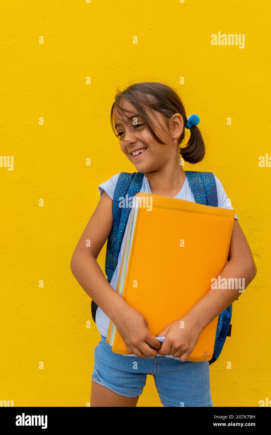 Une fille de race blanche est très heureuse de retourner de l'école, avec son dossier jaune et son fond jaune. Concept de retour à l'école Banque D'Images