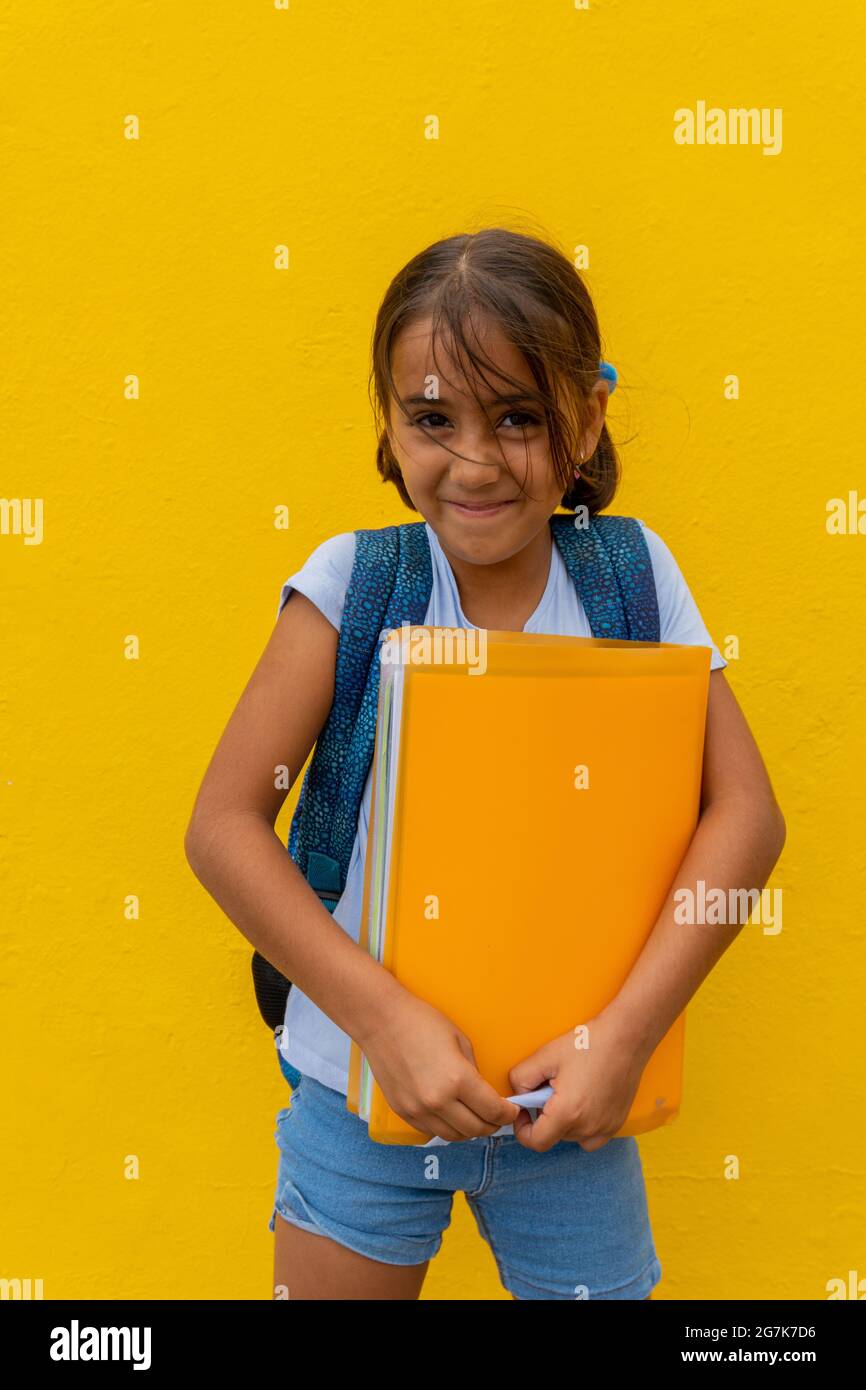 Une fille de race blanche est très heureuse de retourner de l'école, avec son dossier jaune et son fond jaune. Concept de retour à l'école Banque D'Images