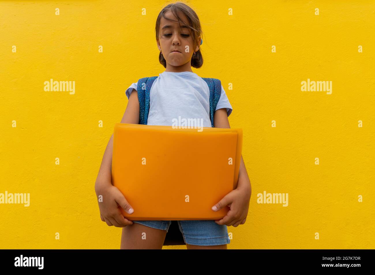 Écolière avec un dossier jaune et un fond, très sérieux au sujet de retourner à l'école. Banque D'Images