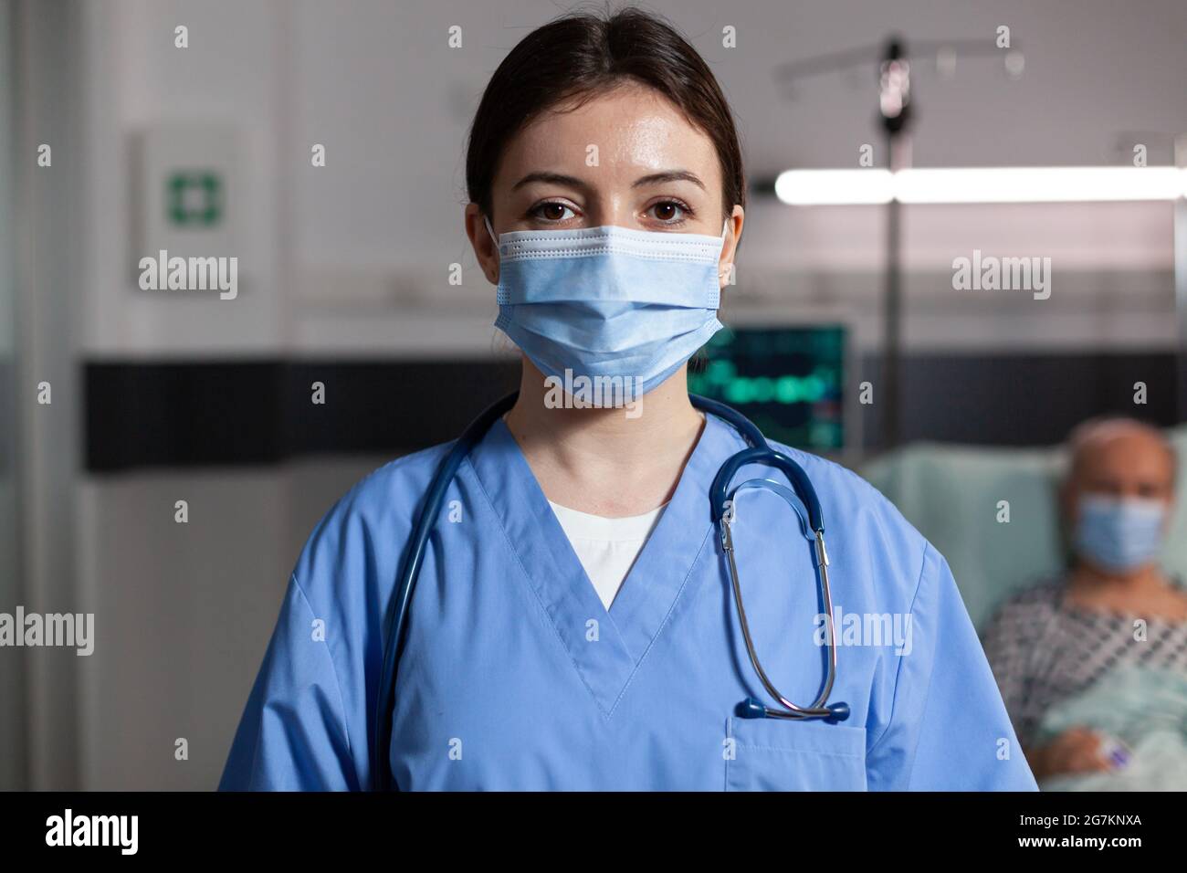 Médecin spécialiste des soins de santé portant un masque de chirurgie dans  la chambre d'hôpital regardant la caméra avec la respiration malade du  patient avec l'aide d'un tube d'oxygène et d'une goutte