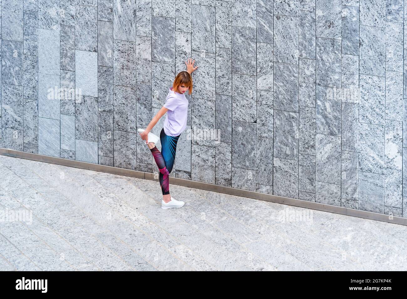 Femme athlétique travaillant en ville réchauffant ses muscles en faisant des exercices d'étirement de jambe dans un passage à côté d'un bâtiment commercial dans un Health A. Banque D'Images