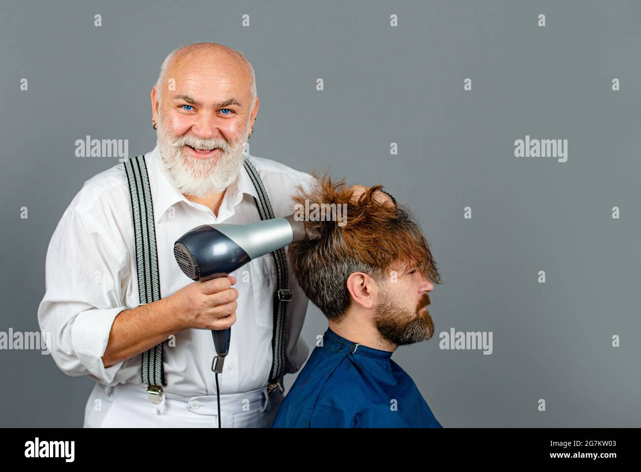 Homme barbu obtenir la coiffure par coiffure avec sèche-cheveux au  barbershop. Coiffeur heureux tenant un sèche-cheveux Photo Stock - Alamy
