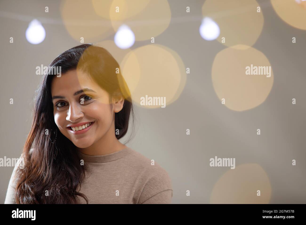 UNE JEUNE FEMME HEUREUSE SOURIANT ET REGARDANT LA CAMÉRA AVEC DES LUMIÈRES AUTOUR Banque D'Images