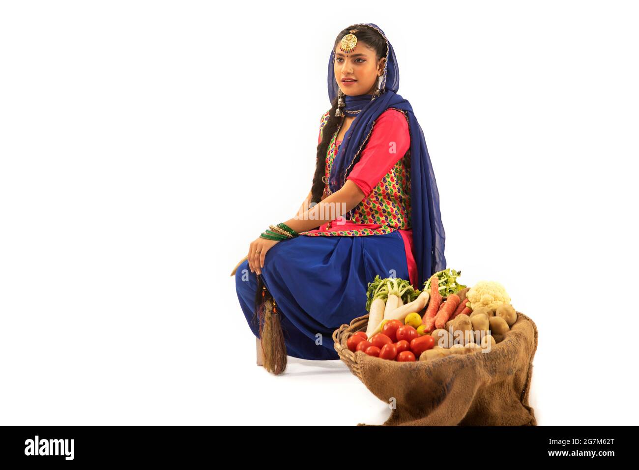 Une femme en costume de Giddha assise avec un panier de légumes à ses côtés. Banque D'Images