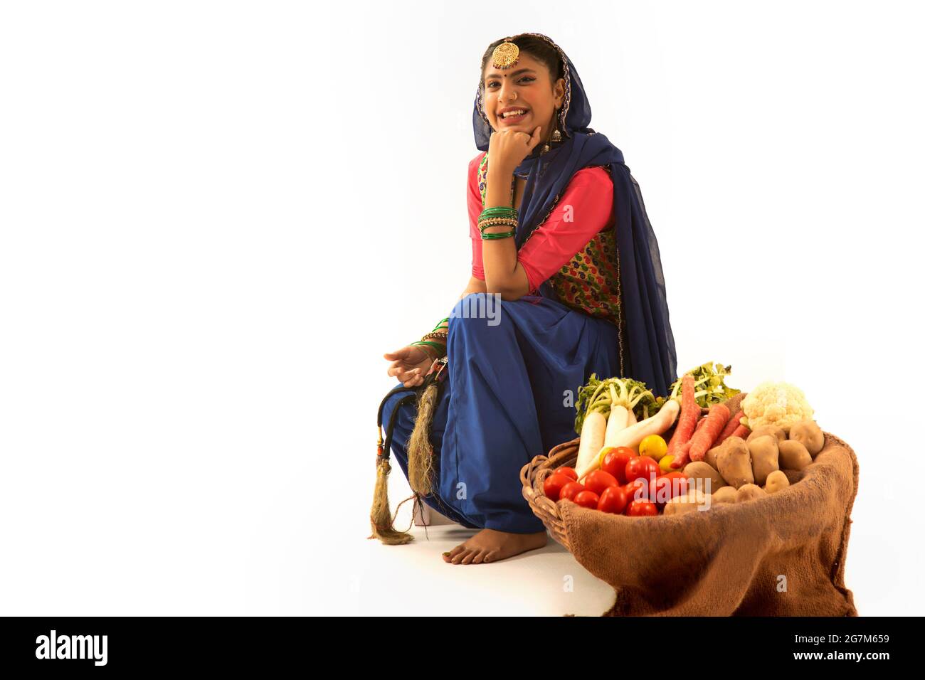 Une femme en costume de Giddha assise avec un panier de légumes à ses côtés. Banque D'Images Une femme en costume de Giddha assise avec un panier de légumes à ses côtés. Banque D'Images