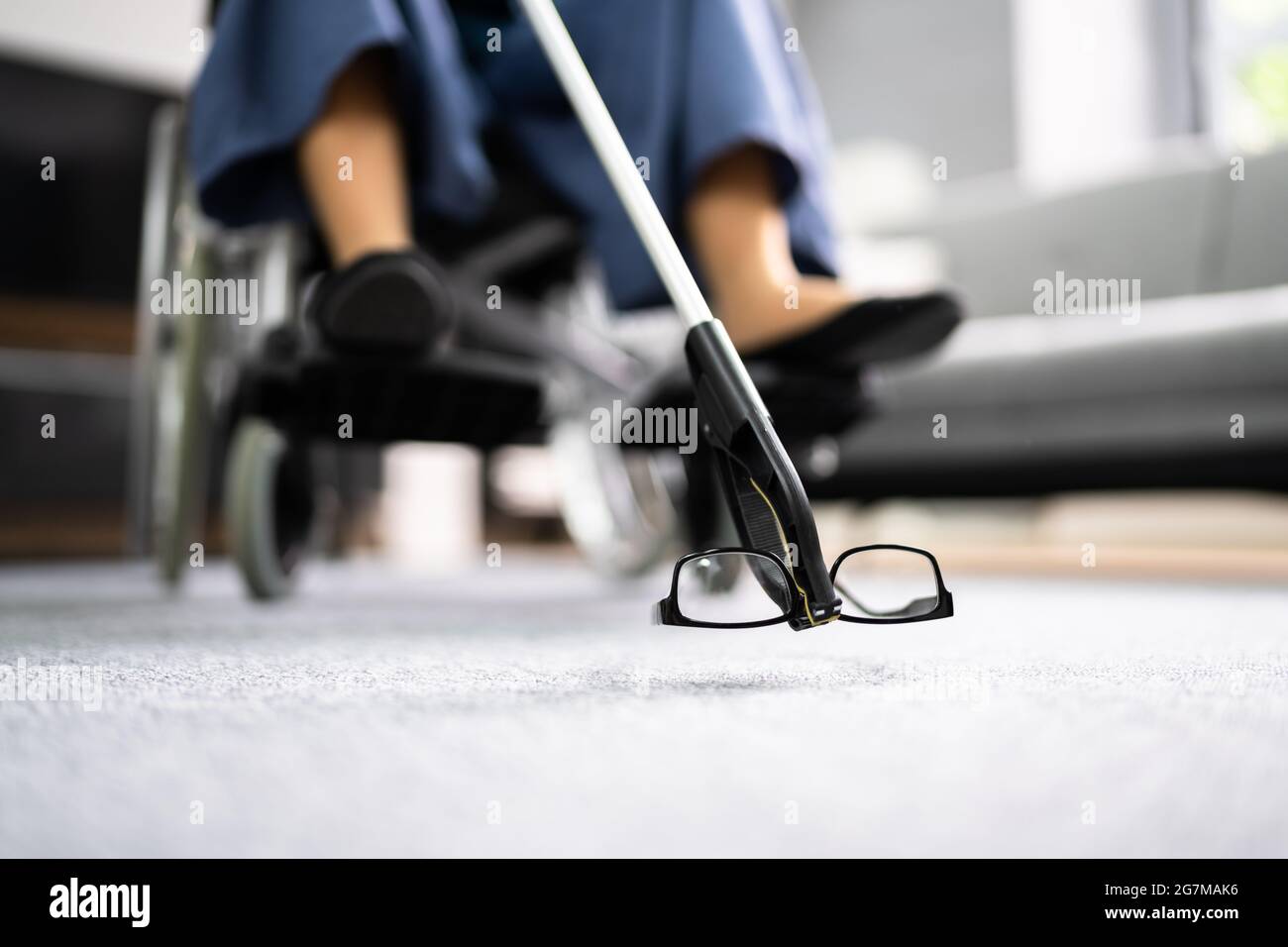 Femme handicapée en fauteuil roulant utilisant l'outil à pince ou Reacher pour les lunettes tombées Banque D'Images