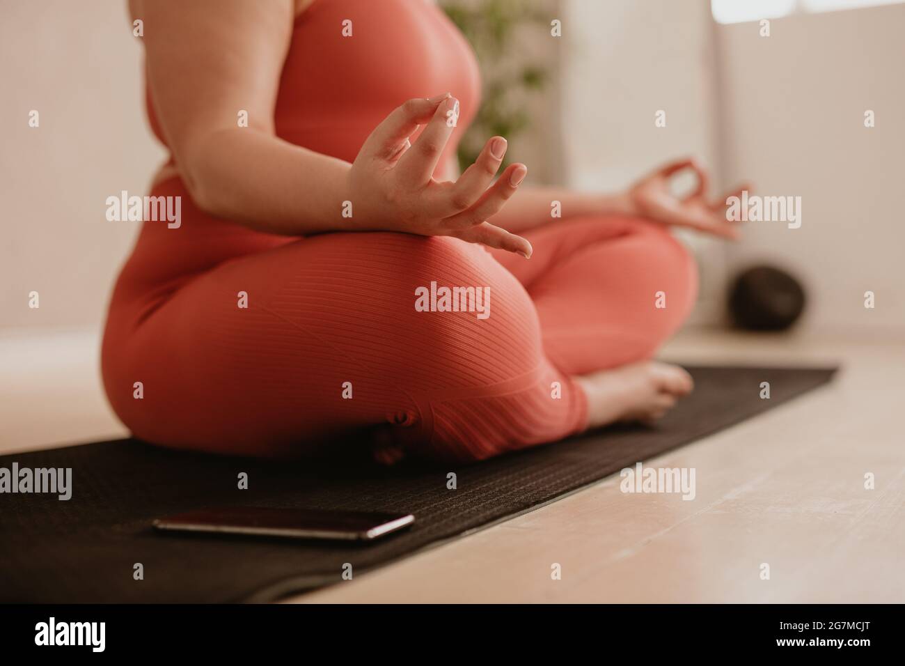 Femme assise sur un tapis de fitness avec les jambes croisées et les mains sur les genoux en posture de yoga. Femme méditant dans la pose de lotus à la salle de gym. Banque D'Images
