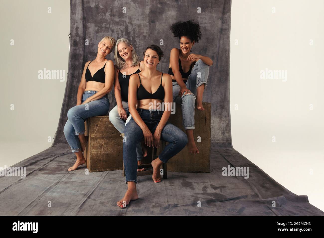 Photo en studio de différentes femmes qui embrassent leur corps naturel. Quatre femmes positives de corps de différents âges souriant gaiement tout en portant des jeans. Femmes Banque D'Images