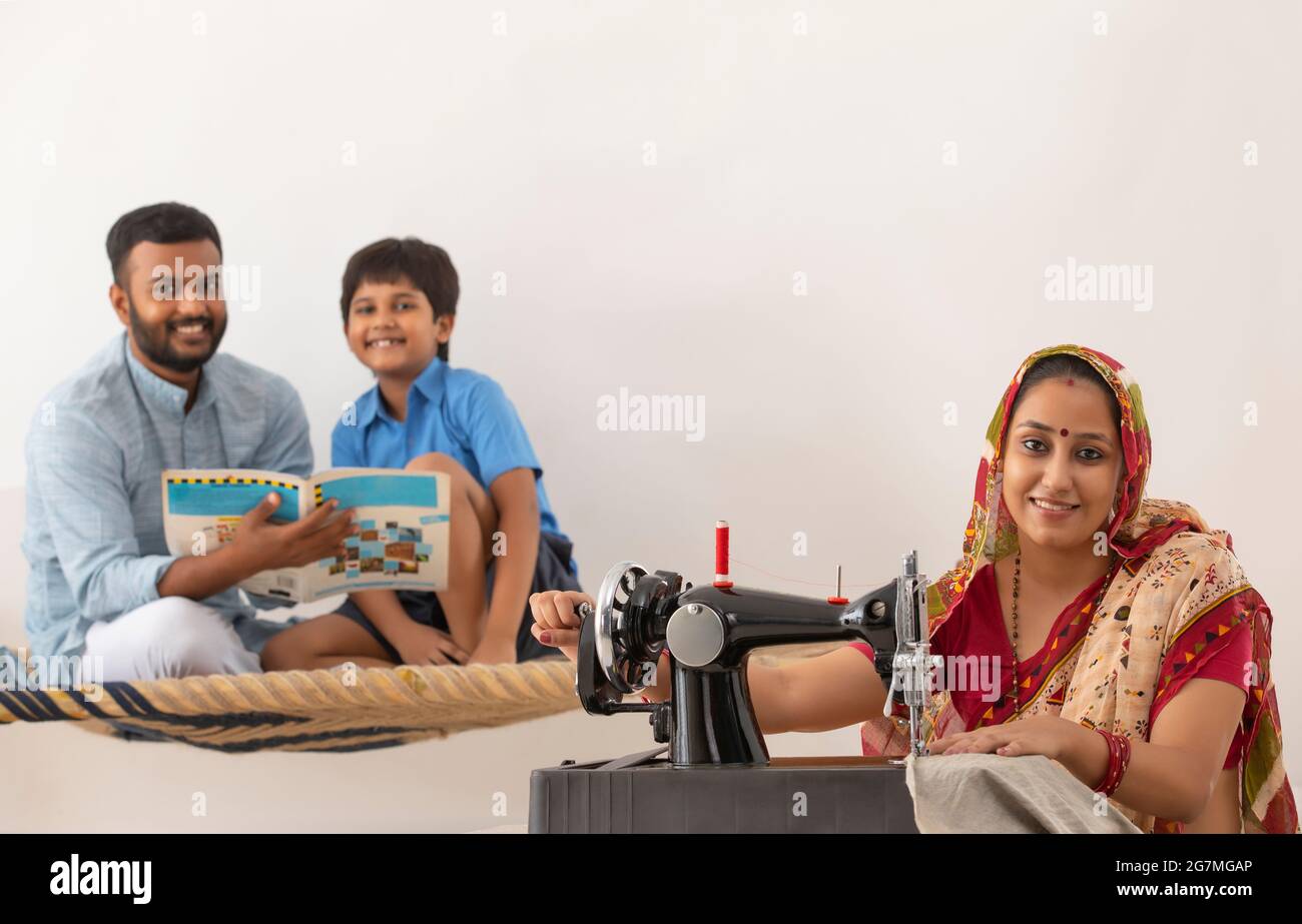 PORTRAIT D'UNE FEMME RURALE SOURIANT ET REGARDANT L'APPAREIL PHOTO AVEC SON MARI ET SON FILS DERRIÈRE ASSIS ET POSANT Banque D'Images