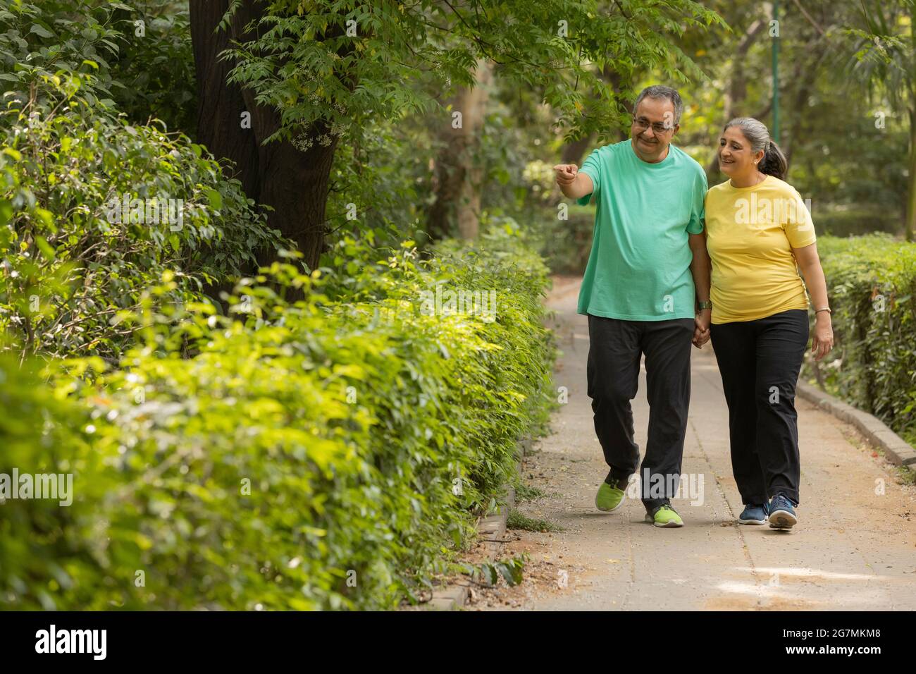 UN MARI ADULTE SENIOR POINTANT VERS LE JARDIN TOUT EN MARCHANT AVEC SA FEMME Banque D'Images