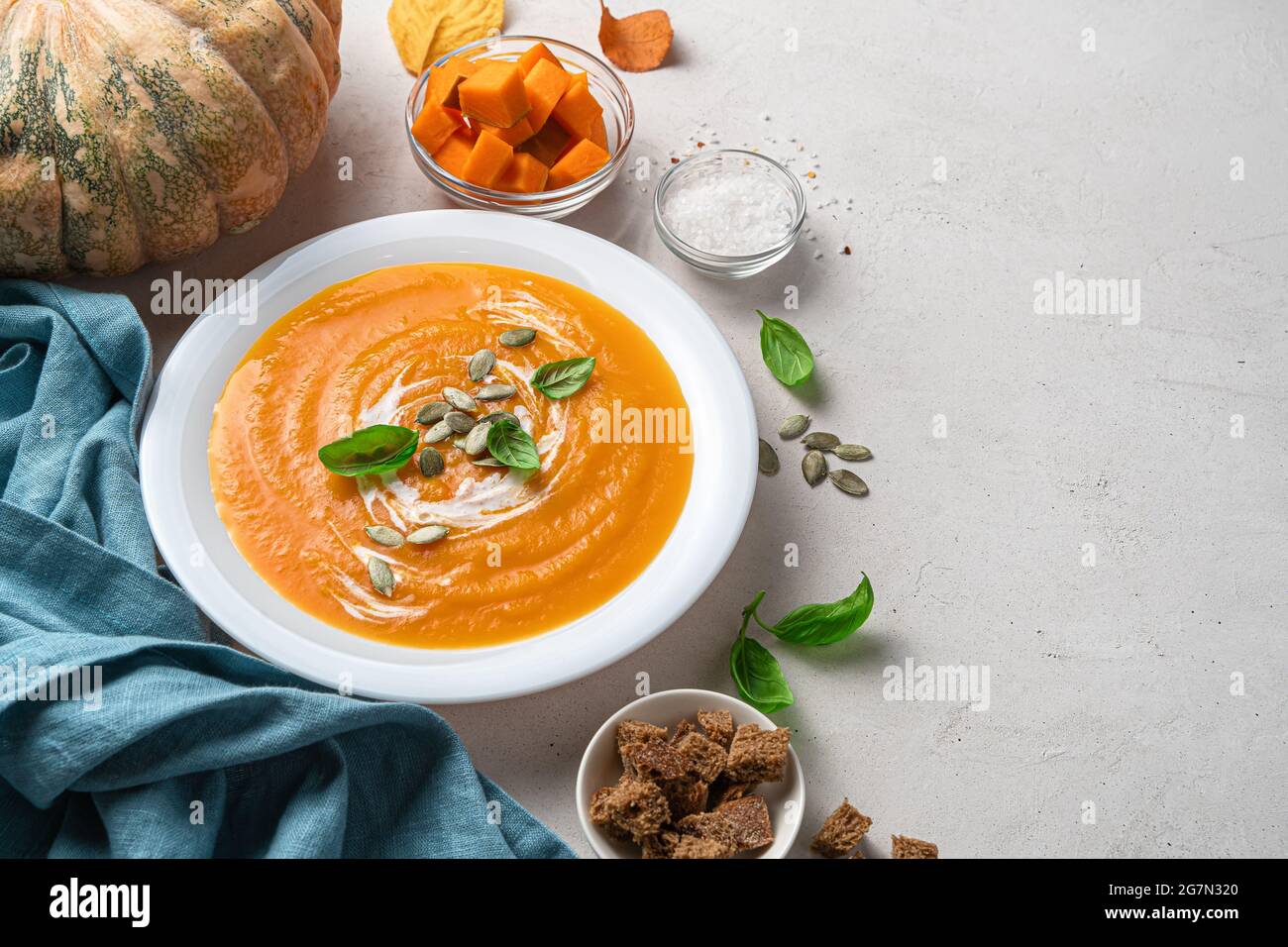 Soupe de potiron d'automne dans une assiette blanche sur fond gris avec potiron, épices et craquelins de seigle. Banque D'Images