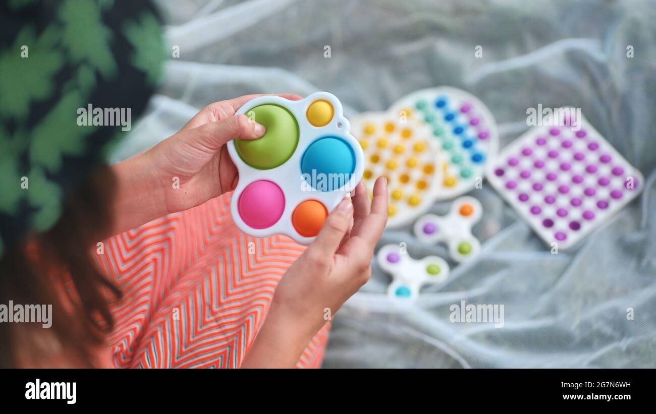 Une jeune fille joue avec des jouets multicouleurs anti-stress popit et des fossettes simples dans le parc lors d'une journée d'été. Banque D'Images