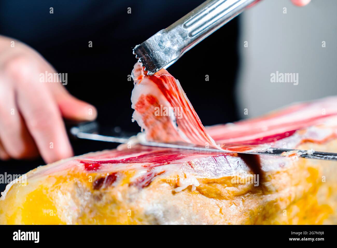 Personne anonyme coupant une jambe de jambon ibérique à 100% et tenant avec des brucelles une tranche appétissante et délicieuse de jambon ibérique. Jambon ibérique nourri à l'Acorn. Type Banque D'Images