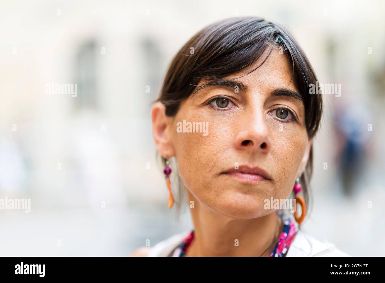 Pousse-tête de jeune femme sûre et attrayante avec de longs cheveux foncés et des yeux bleus à l'extérieur, regardant loin avec une expression sérieuse sur son visage Banque D'Images