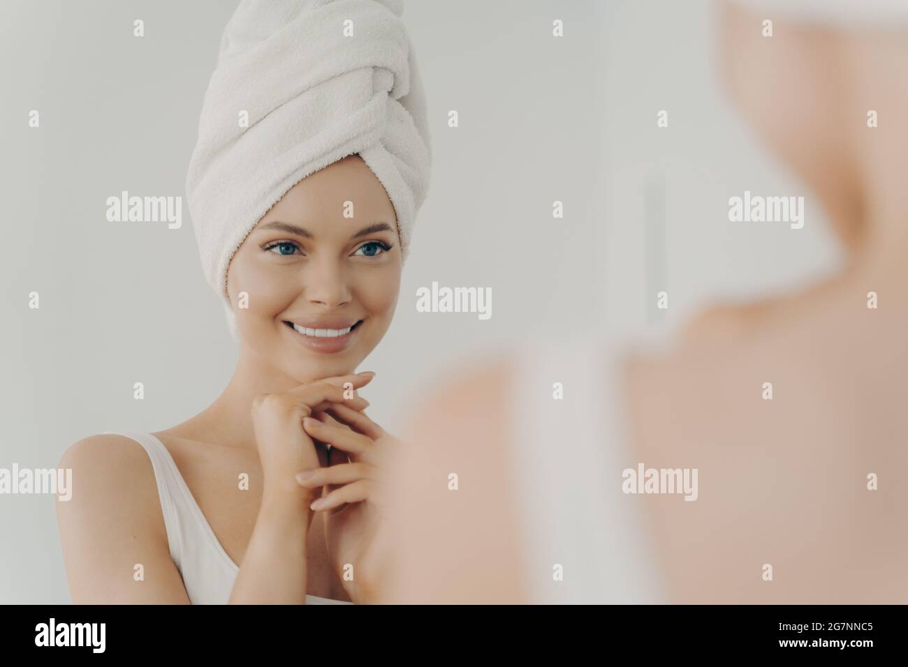 Jeune femme en bonne santé avec une peau propre souriant tout en appliquant de la crème pour le visage Banque D'Images