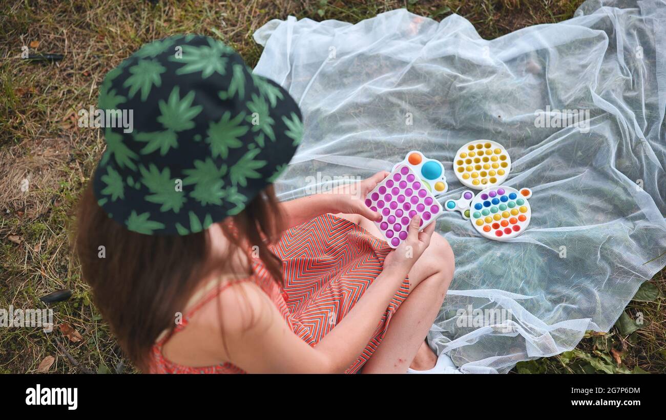 Une jeune fille joue avec un popit anti-stress et des jouets simples à fossettes dans le parc lors d'une journée d'été. Banque D'Images