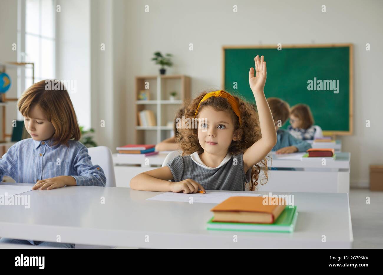 L'élève de l'école primaire lève la main, prête à répondre aux questions de l'enseignante en classe. Banque D'Images