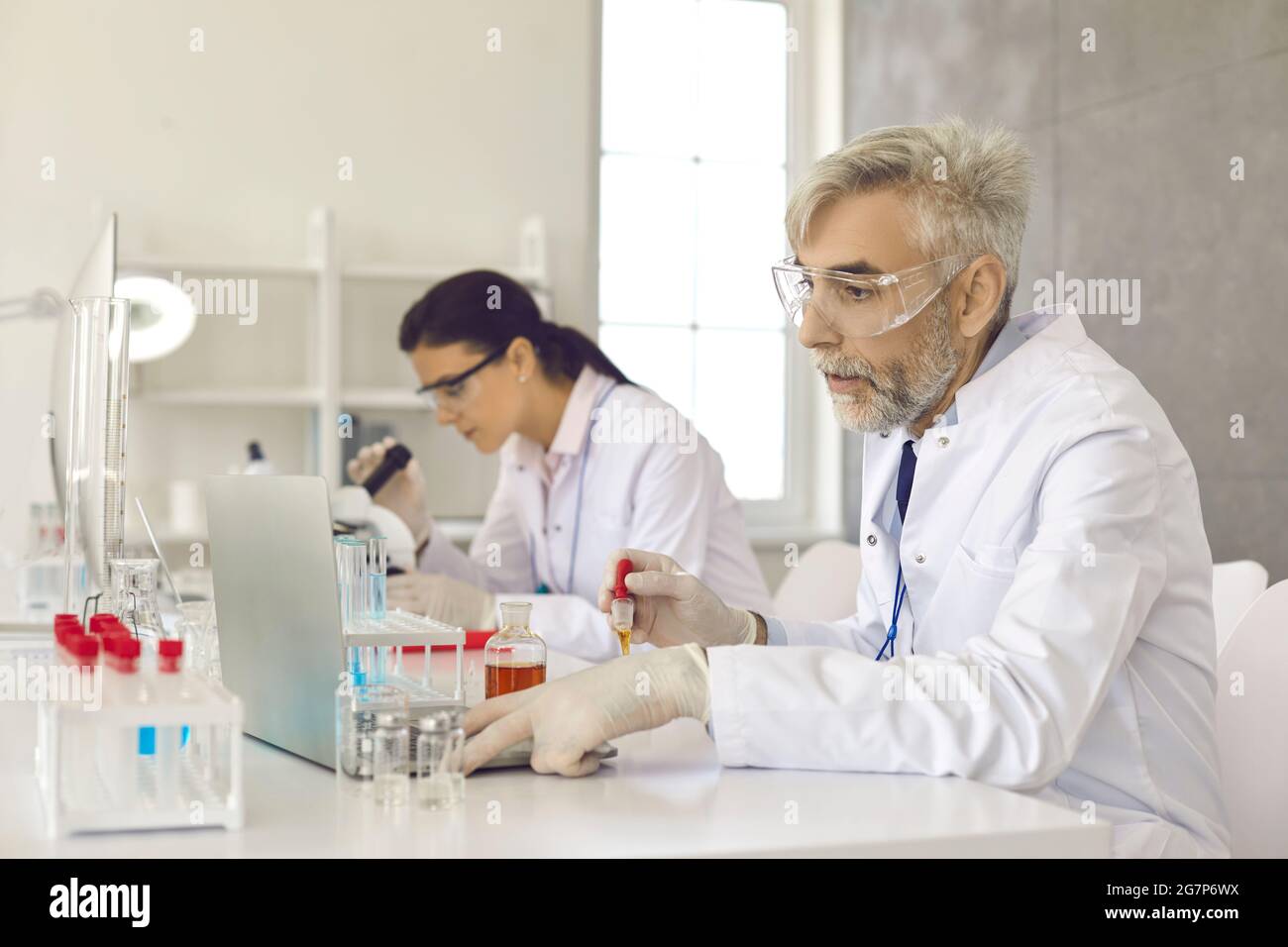 Un scientifique sérieux utilisant un ordinateur portable tout en travaillant sur un nouveau vaccin en laboratoire médical Banque D'Images