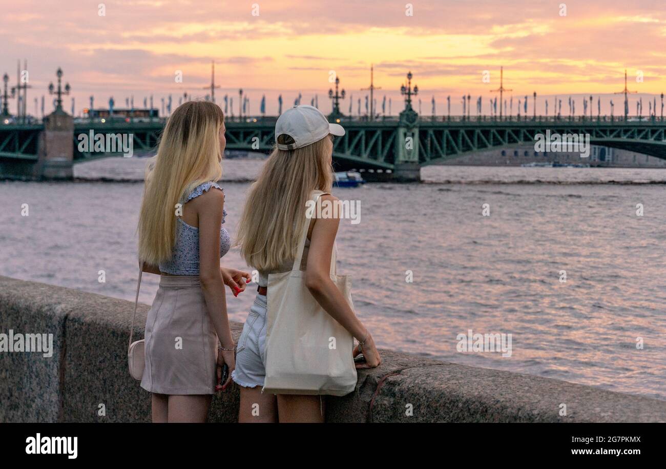 Deux jeunes femmes debout et penchées sur le granit du remblai, profitant de la vue sur le coucher du soleil sur la rivière Neva, pendant la nuit blanche, Saint-Pétersbourg Banque D'Images