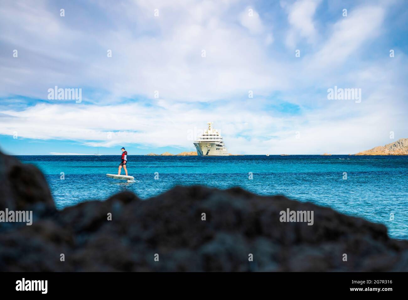 (Mise au point sélective) vue imprenable sur un yacht de luxe naviguant sur une eau turquoise tandis qu'un touriste défoqué est sur un hydroptère électrique. Banque D'Images
