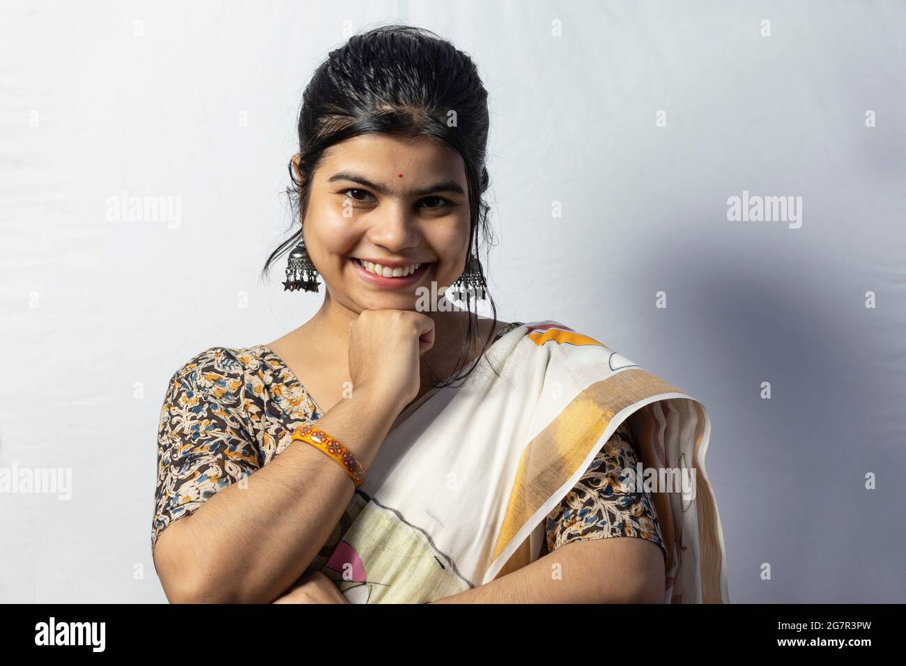 Isolée sur fond blanc une femelle indienne en saree sourit à l'appareil photo avec la main sous le menton pose sur fond blanc Banque D'Images