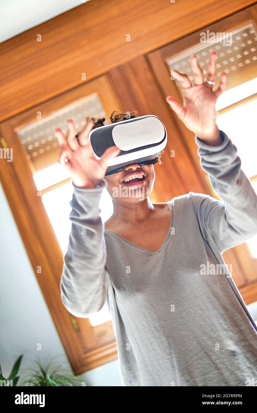 Portrait d'une jeune femme noire active qui teste un simulateur de réalité virtuelle dans une pièce à la maison. Technologies et concepts de style de vie. Banque D'Images