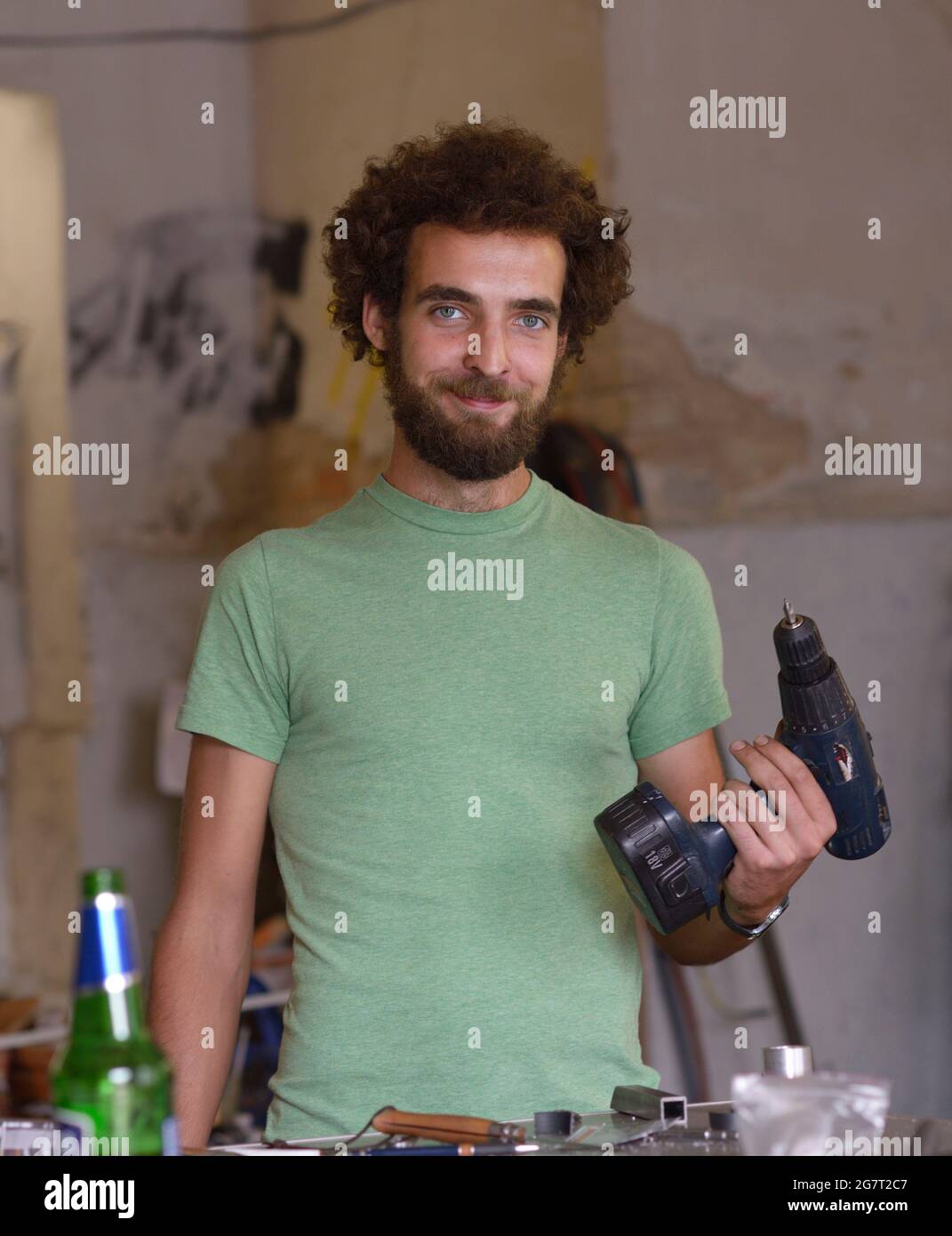 Jeune réparateur barbu souriant debout sur la table de travail avec un exercice dans la main à son atelier de réparation de vélo. 23 juillet 2019. Kiev, Ukraine Banque D'Images