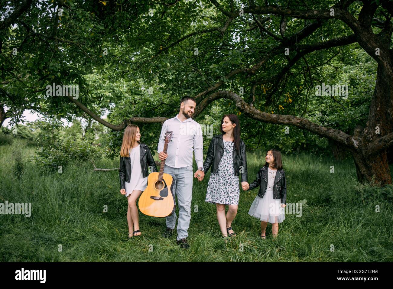 Portrait complet de la belle famille caucasienne dans des vêtements d'été élégants tenant les mains et marchant dans le jardin vert. Les parents avec deux enfants passent du temps sur la nature. Banque D'Images