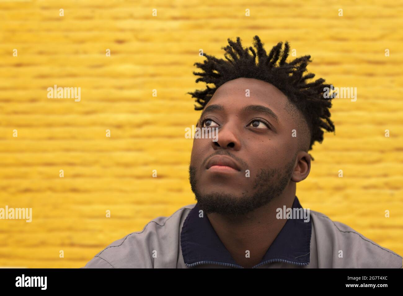 Un jeune Africain confident regarde devant lui tout en étant assis devant un mur jaune Banque D'Images