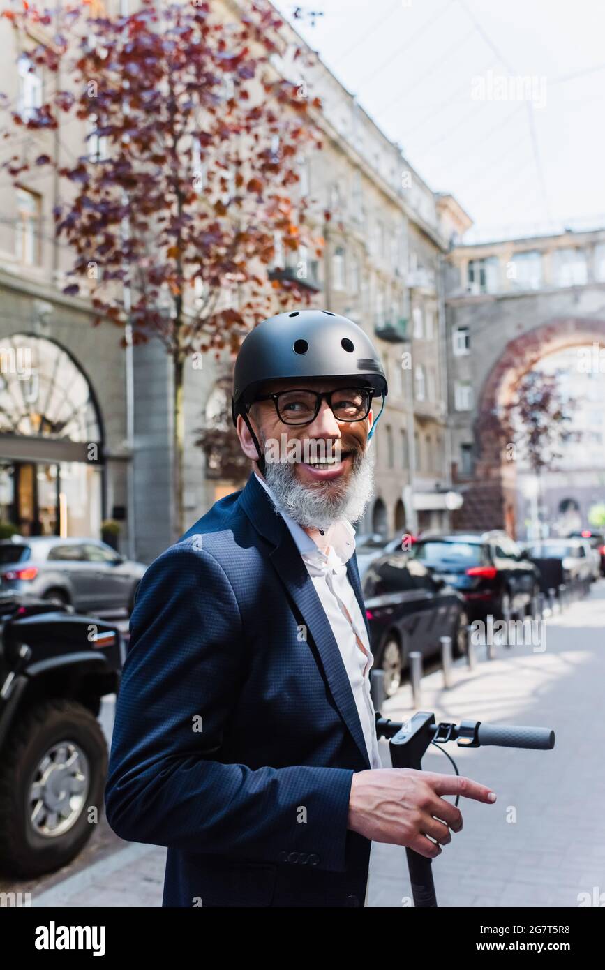 homme d'affaires joyeux et mature dans blazer et casque de scooter électrique Banque D'Images