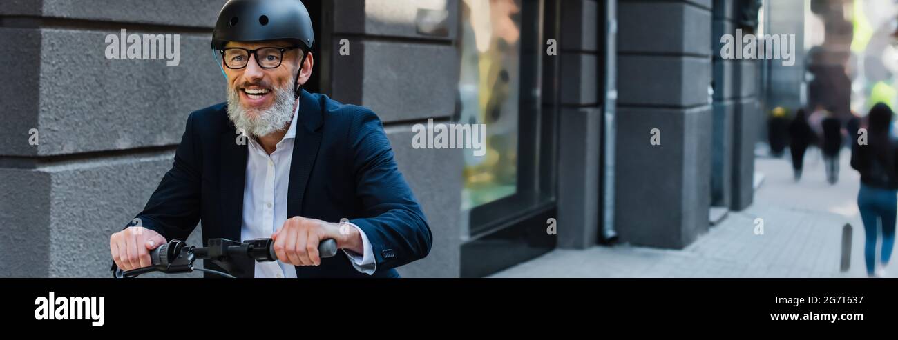 joyeux homme d'affaires mature dans blazer et casque à cheval e-scooter, bannière Banque D'Images