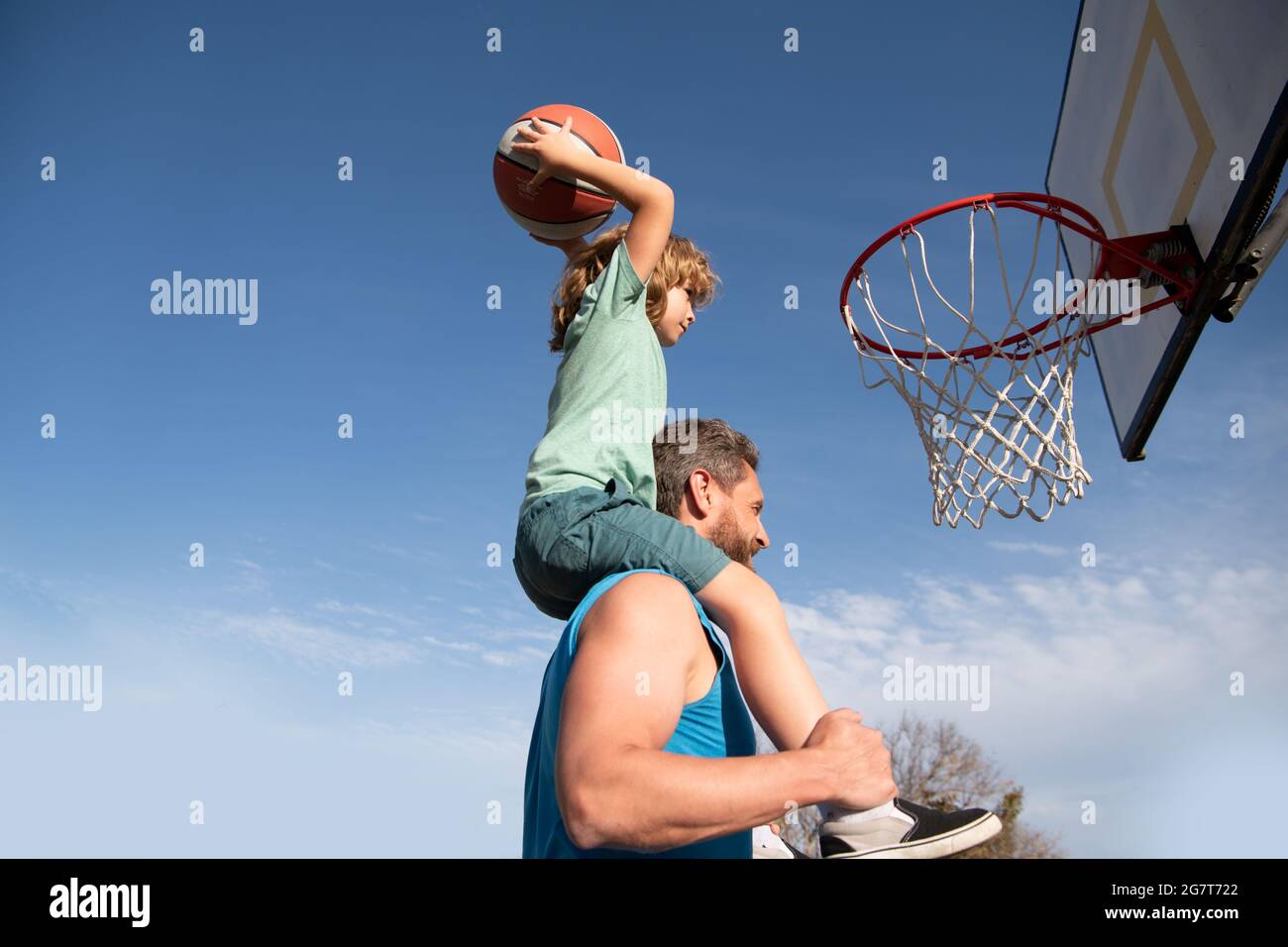 Père et fils jouant au basket-ball. Un père heureux tenant son petit fils  sur les épaules, l'aidant à marquer un panier sur un terrain de basket-ball.  Copier Photo Stock - Alamy
