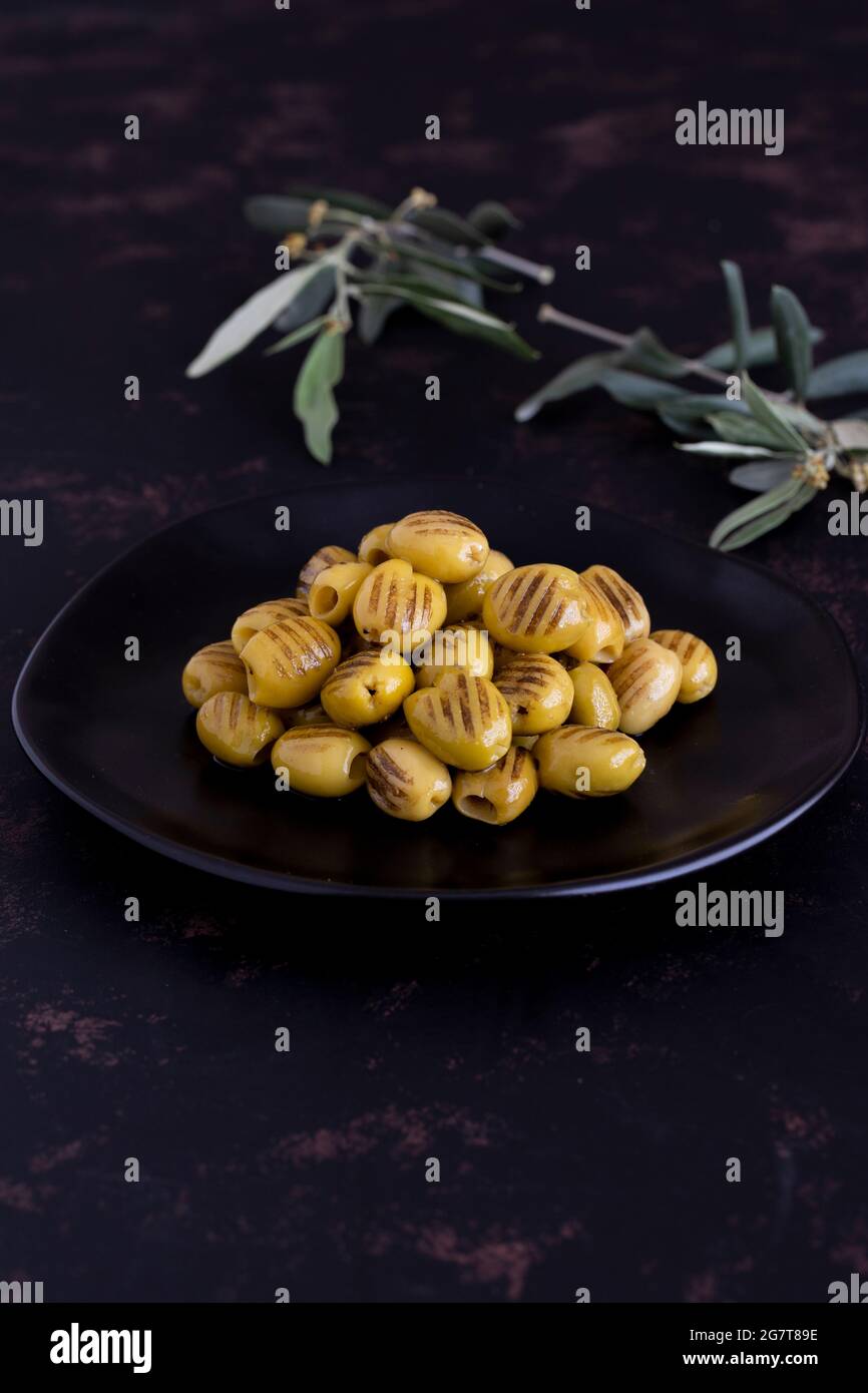 Olives vertes grillées sur fond sombre. De savoureuses olives vertes grillées dans le bol Banque D'Images