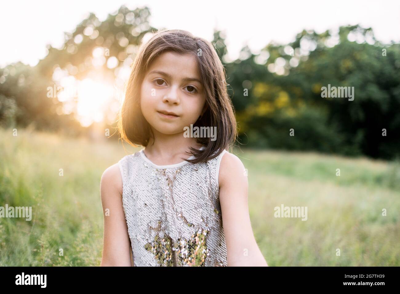 Portrait d'une jolie petite fille aux cheveux bruns courts posé au jardin vert avec un beau lever de soleil derrière. Concept de bonheur et d'enfance. Banque D'Images