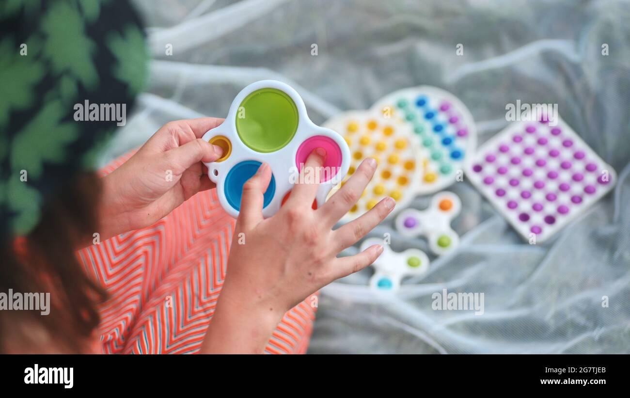 Une jeune fille joue avec des jouets multicouleurs anti-stress popit et des fossettes simples dans le parc lors d'une journée d'été. Banque D'Images