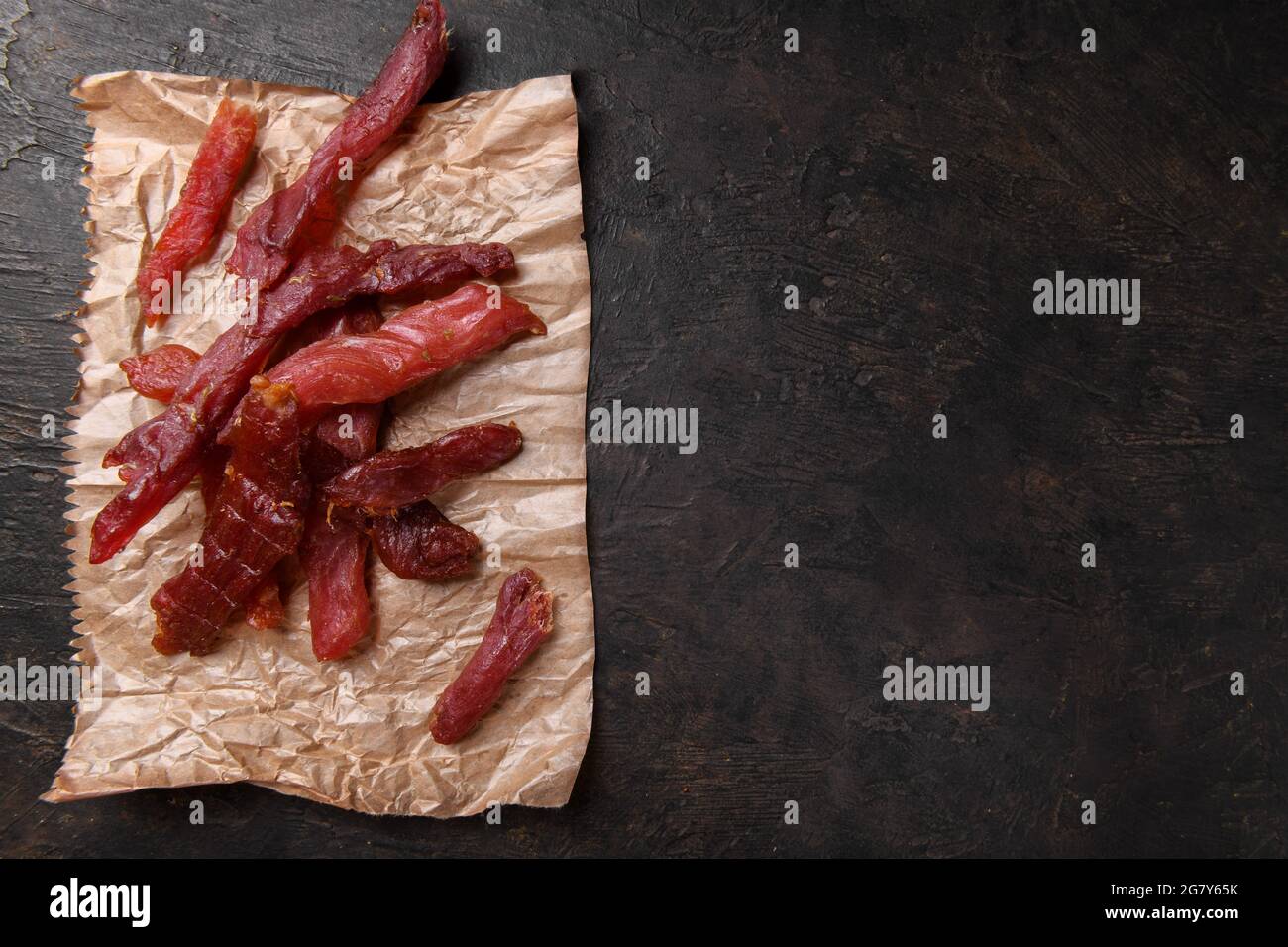 Bandes de viande jerky avec épices et herbes sur un papier sur fond sombre. La copiette de cuisine italienne typique est une bande de viande de porc épicée. En-cas pour bières, Banque D'Images