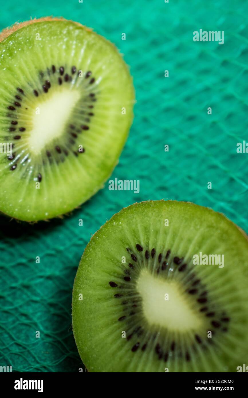 Gros plan de deux parties de kiwi fraîchement coupées sur une surface texturée verte Banque D'Images