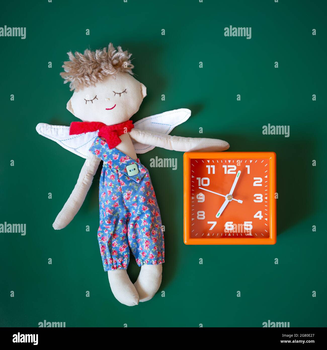 Jouet ange endormi et réveil orange sur fond vert foncé. Concept de l'heure de se réveiller ou d'aller au lit, ne soyez pas en retard. Jouets de couture Banque D'Images