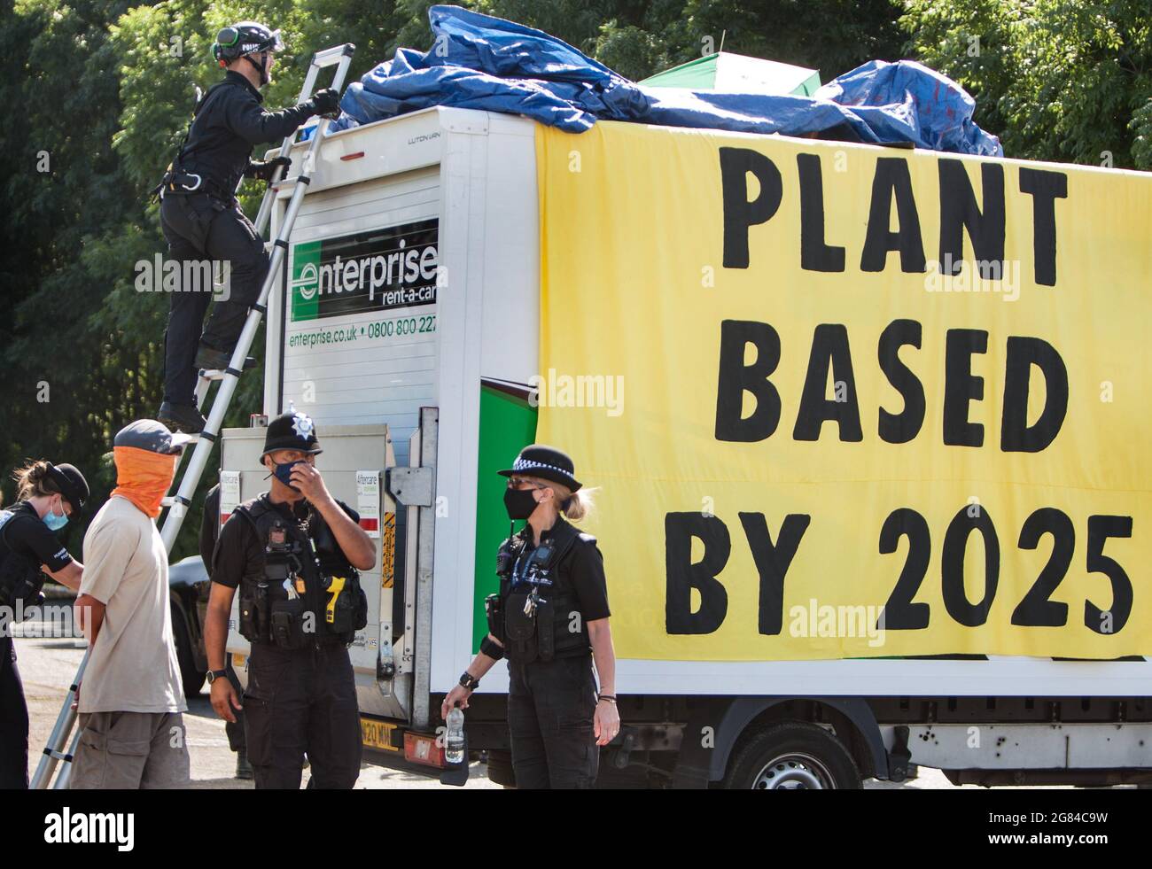 Scunthorpe, Royaume-Uni. 16 juillet 2021. Un policier spécialisé pèse une échelle pour enlever les rebelles attachés ensemble sous une bâche au-dessus d'une fourgonnette avec une bannière intitulée « Plant based by 2025 » pendant la manifestation. Plus de 50 manifestants de la rébellion animale ont fermé la seule usine de distribution de hamburgers de McDonald's, l'usine OSI Food Solutions au Royaume-Uni, en blockant l'entrée avec des balises en bambou et des véhicules. Les rebelles exigent que McDonald's passe à des menus entièrement basés sur des plantes d'ici 2025 et mette fin à la souffrance de milliards de vies et pour éviter la crise climatique tout en sauvant la forêt amazonienne. Crédit: SOPA Banque D'Images