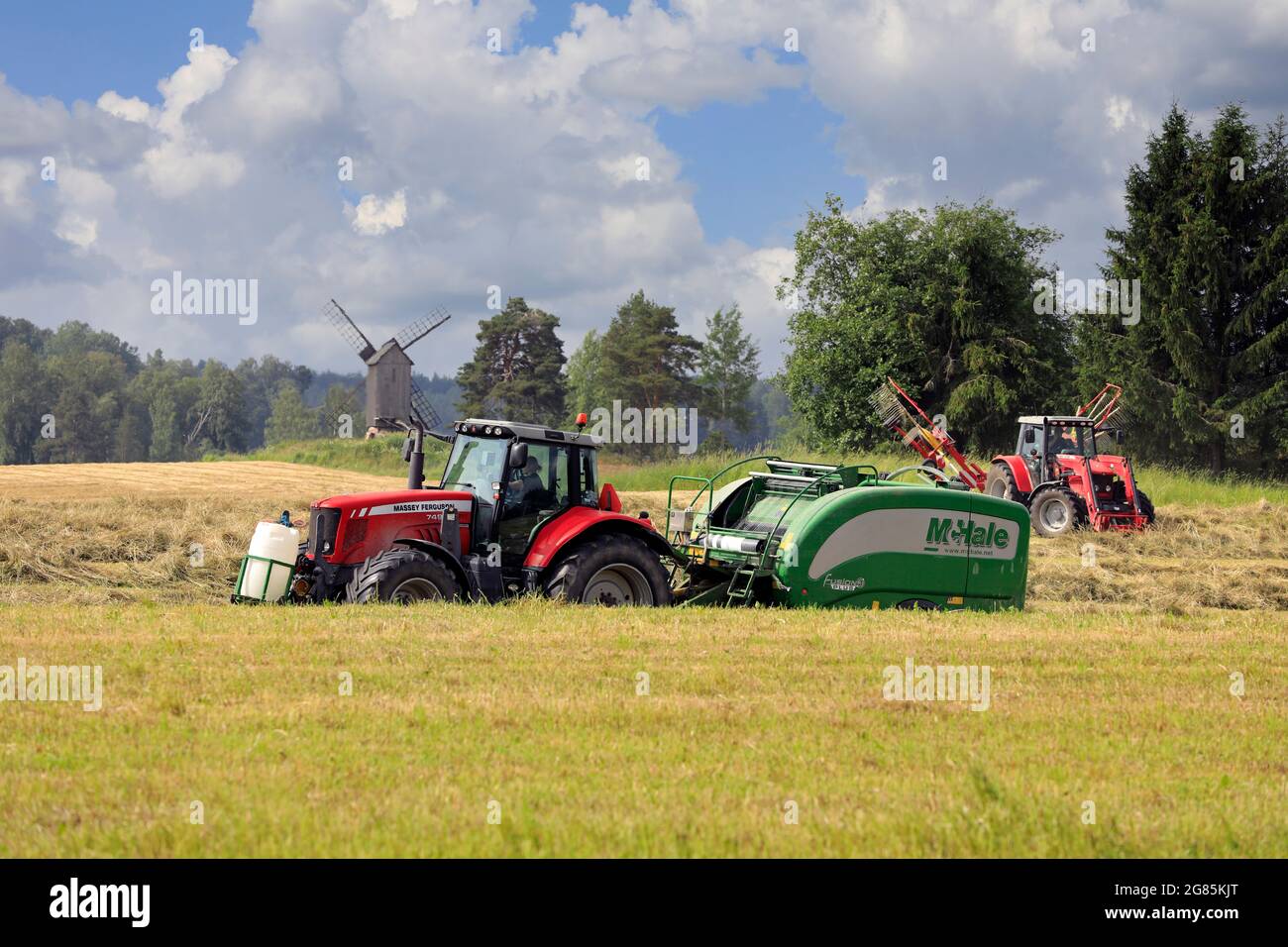 Tracteurs Massey-Ferguson dans le champ de foin avec enrubanneuse à ramasseuse-presse McHale et peigne rotatif pour la récolte de foin sec en été. Raasepori, Finlande. 25 juin 2021. Banque D'Images