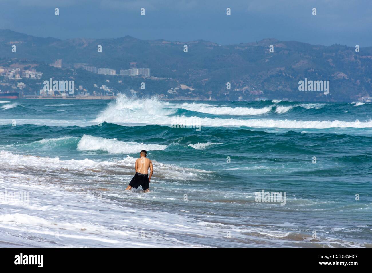 Vue arrière d'un jeune garçon arabe debout dans la mousse de mer de la plage Jeanne d'arc Banque D'Images