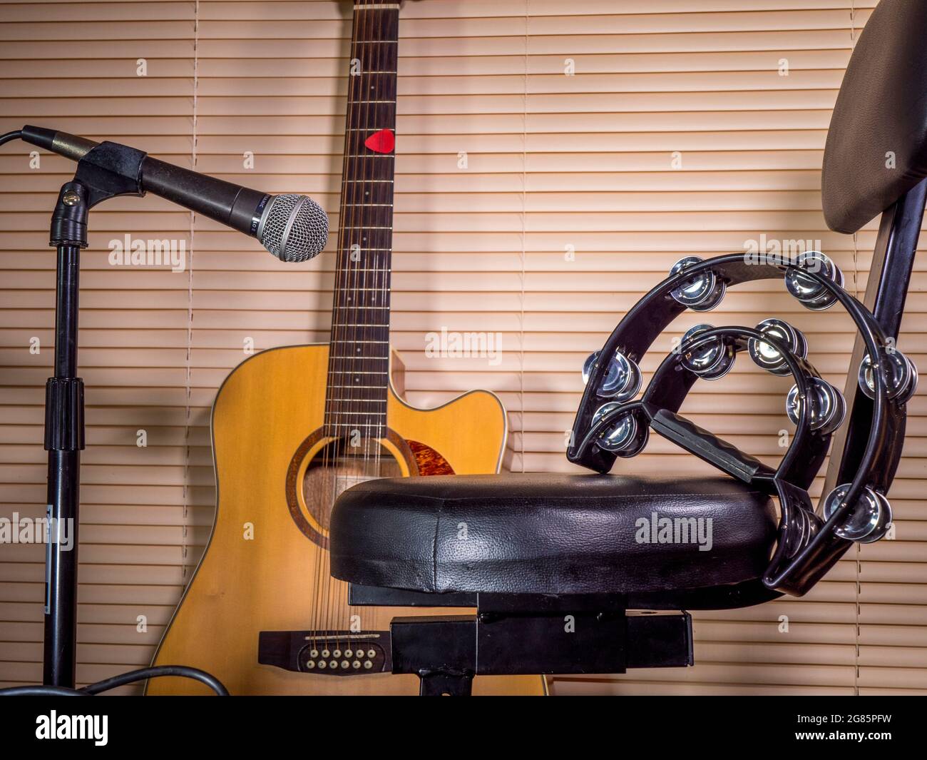 Un tambourin sur le siège rembourré d'un tabouret / chaise de performance musicale, avec une guitare acoustique et un microphone sur un stand à proximité. Banque D'Images