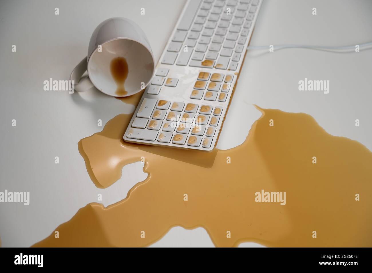 Tasse de café noir renversée sur le clavier de l'ordinateur sur la table blanche. Banque D'Images Tasse de café noir renversée sur le clavier de l'ordinateur sur la table blanche. Banque D'Images