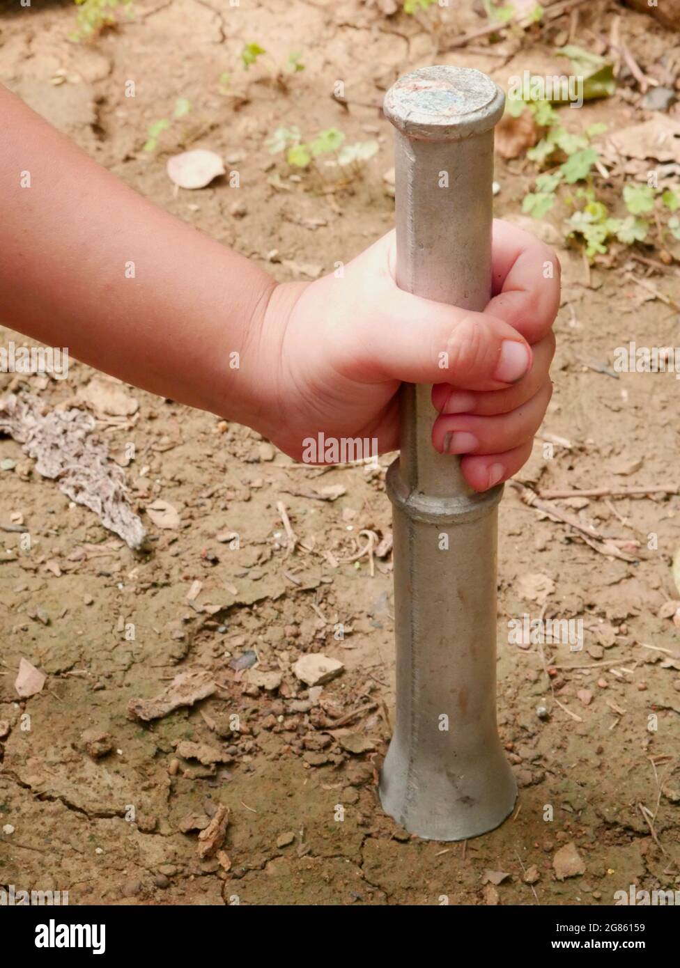 Main d'enfant tenant des outils de construction en fer tout en frappant le sol. Banque D'Images