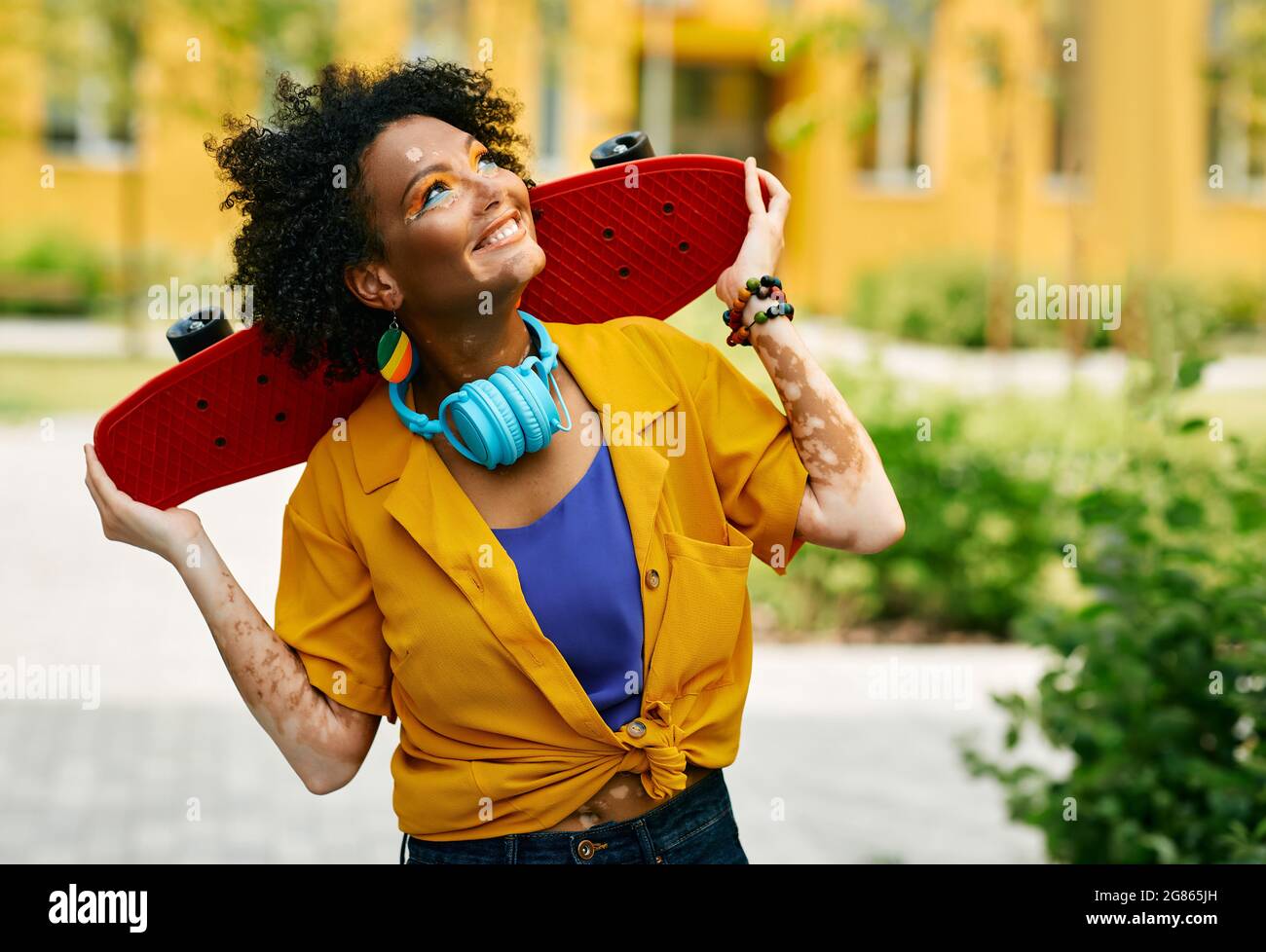 Une femme multi-ethnique aux cheveux bouclés tient le skateboard pendant la marche de la ville moderne en appréciant les loisirs d'activités estivales Banque D'Images