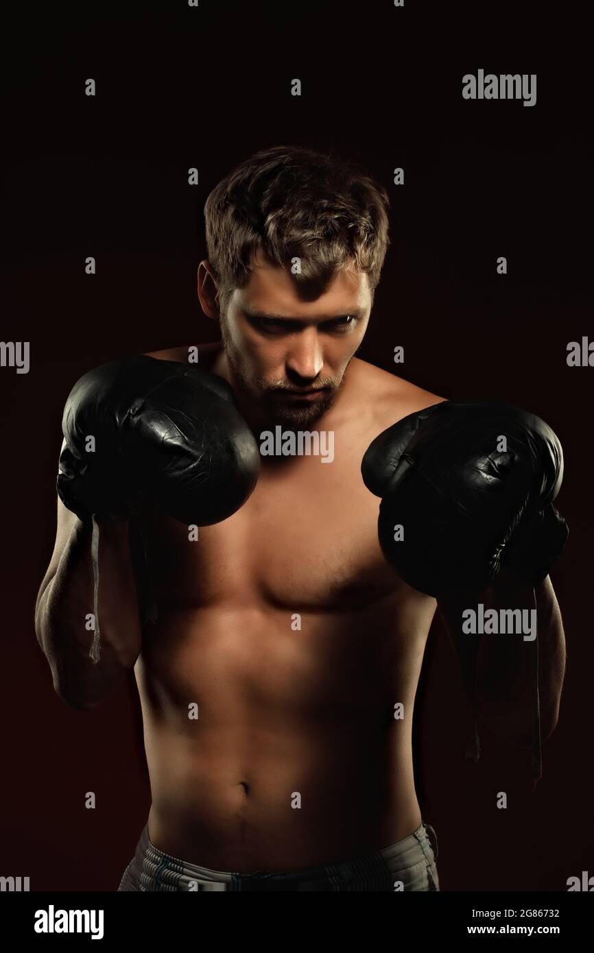 Voici un portrait spectaculaire d'un boxeur en vieux gants de boxe sur fond sombre. Un combattant athlétique des arts martiaux mixtes se tient en position de combat. Bannière pour les événements sportifs. Banque D'Images