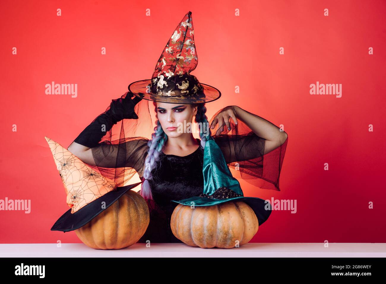 Belle jeune femme surprise en sorcières chapeau et costume tenant la citrouille. Femme de beauté posant avec la citrouille et le chapeau d'Halloween. Robes d'Halloween et Banque D'Images